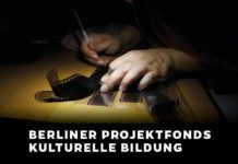 In einer Dunkelkammer kratzt eine Person mit einem Stift in der einen Hand etwas in Foto-Negative hinein. Die andere Hand fixiert die Negative auf einem Tisch.