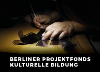 In einer Dunkelkammer kratzt eine Person mit einem Stift in der einen Hand etwas in Foto-Negative hinein. Die andere Hand fixiert die Negative auf einem Tisch.