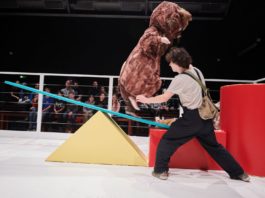 Inszenierungsbild aus "Alarm im Streichelzoo" mit einem Schauspieler im Vordergrund und im Hintergrund ein Mensch im Hamsterkostüm auf einer Wippe