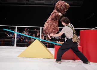 Inszenierungsbild aus "Alarm im Streichelzoo" mit einem Schauspieler im Vordergrund und im Hintergrund ein Mensch im Hamsterkostüm auf einer Wippe