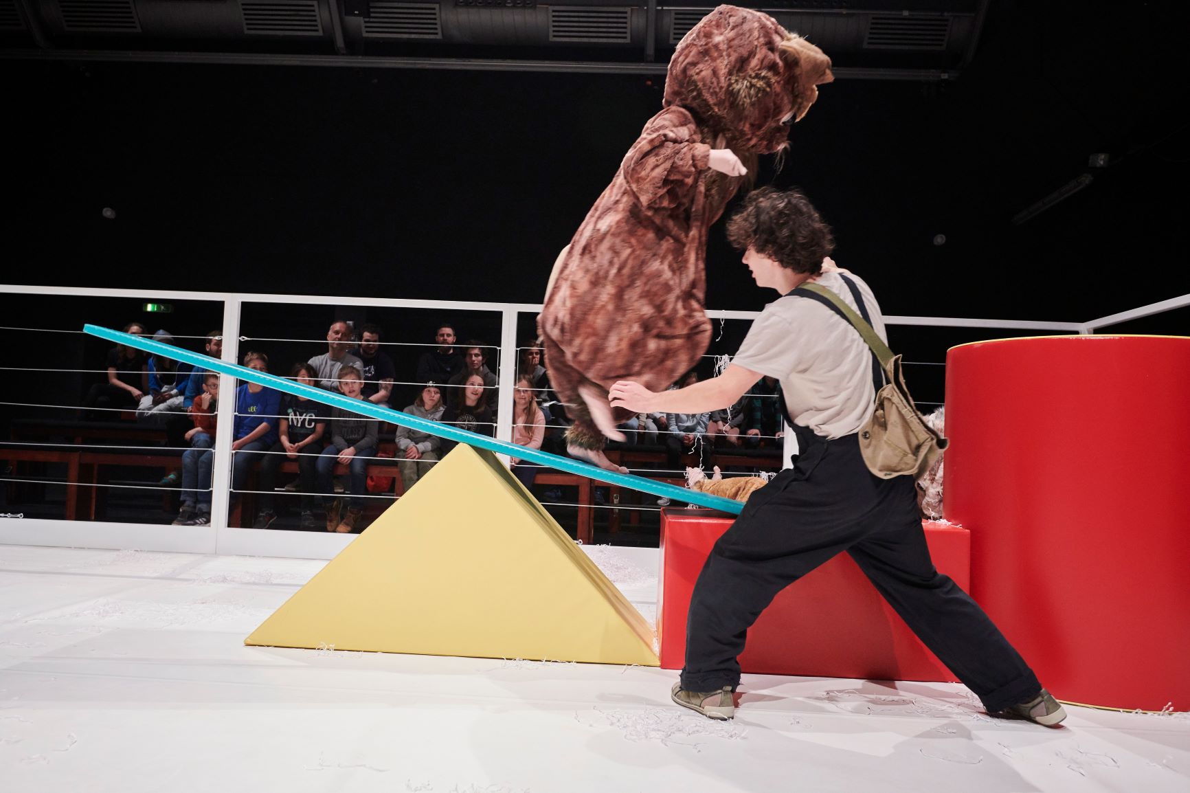 Inszenierungsbild aus "Alarm im Streichelzoo" mit einem Schauspieler im Vordergrund und im Hintergrund ein Mensch im Hamsterkostüm auf einer Wippe