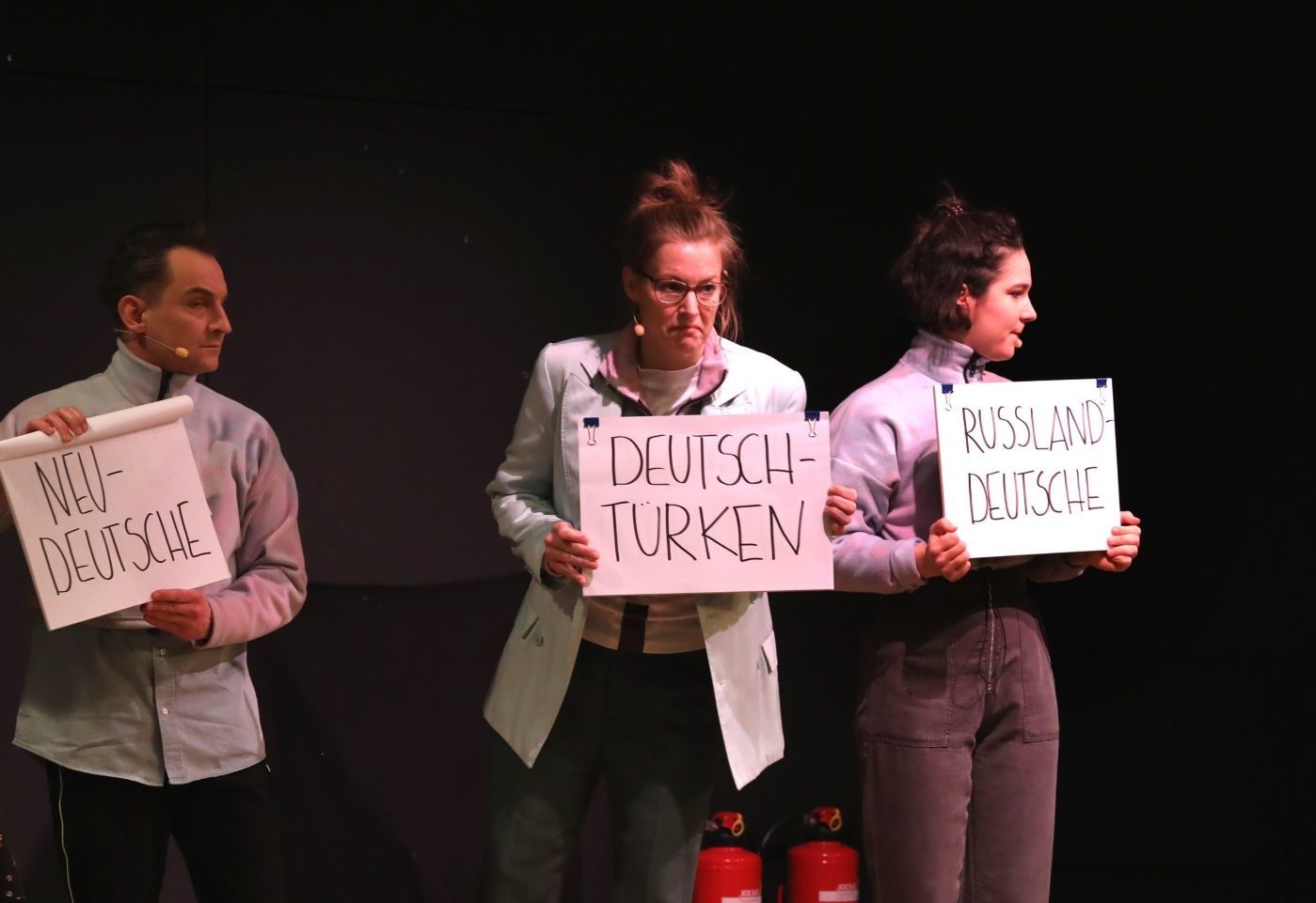 Schauspieler*innen aus "Unterscheidet euch!" auf der Bühne halten Schilder in der Hand, auf der unterschiedliche Begriffe zur Sortierung bzw. Zuordnung stehen.