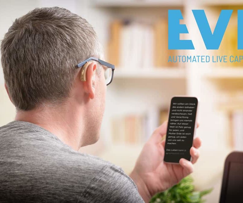 Ein Bild, drinnen, eine Person, sitzend, Mann von hinten mit Hörgerät und Brille auf das Handy schaut, indem er die Untertitel liest. In der rechten Encke oben befindet sich das Logo von EVE mit dem Text "EVE AUTOMATED LIVE CAPTIONS"