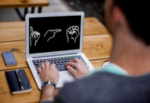 Eine Person sitzt vor einem Laptop, auf dem "DGS" im Fingeralphabet abgebildet ist.