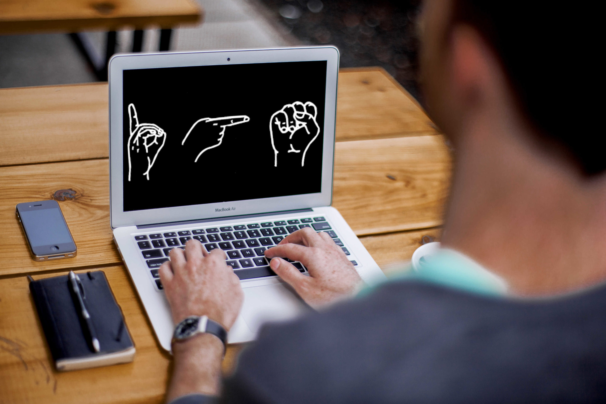 Eine Person sitzt vor einem Laptop, auf dem "DGS" im Fingeralphabet abgebildet ist.