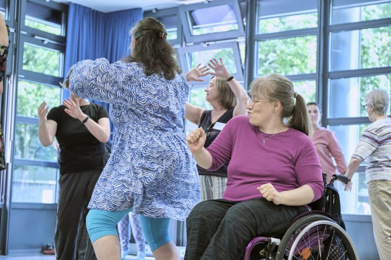 das Bild zeigt tanzende Menschen, eine davon im Rollstuhl