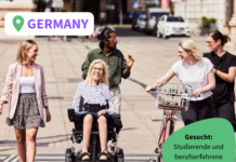 Zwei Personen sitzen nebeneinander am Schreibtisch. Eine Person zeigt auf ihren Bildschirm. Die Andere tippt währenddessen an ihrem Laptop.