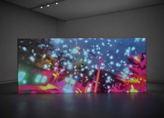 Eine große Leinwand steht in einem abgedunkelten Raum. Auf der Leinwand sind ganz viele weiße Punkte und grelle Farben zu sehen.
