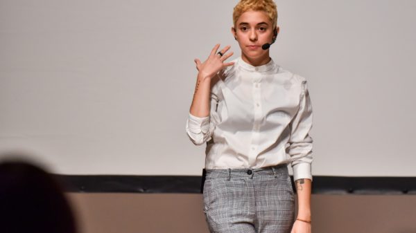 Diana Anselmo steht hell gekleidet vor einer weißen Wand und performt.