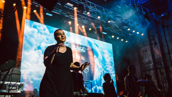 Laura Maaß steht auf der Bühne, im Hintergrund ein Konzert