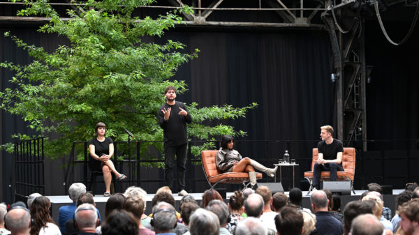 Podiumsgespräch mit DGS-Dolmetscher auf der Bühne bei Brave New Voices in der Jahrhunderthalle Bochum, vor großem Publikum.