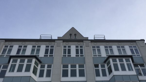 Blick auf das obere Stockwerk der Friedrichstraße 12 und den blauen Himmel dahinter.