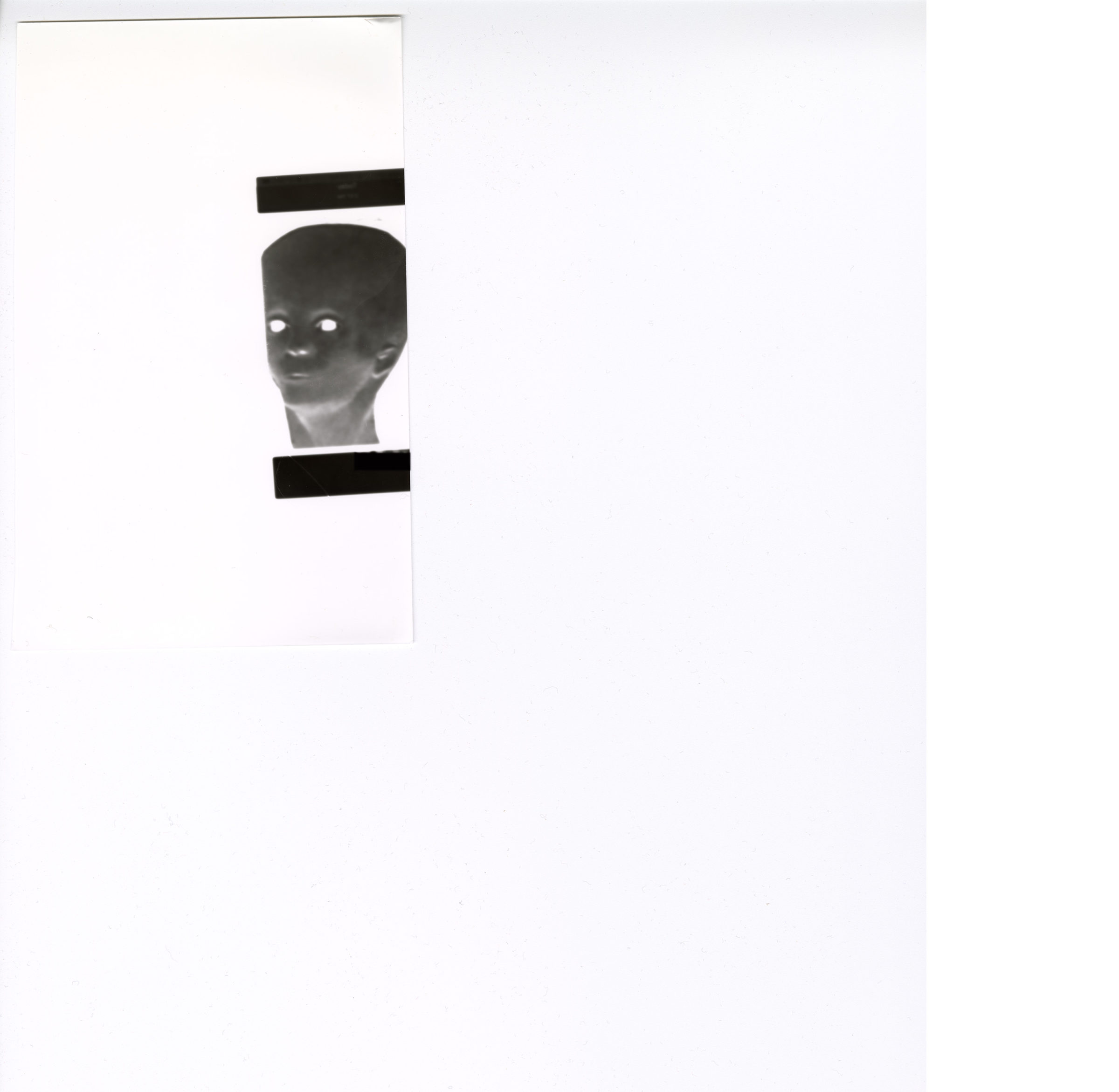 Das Bild zeigt einen weißen Hintergrund mit einer kleinen schwarz-weißen Figur im Negativstil am linken Rand. Die Figur stellt einen Kopf mit leuchtend weißen Augen dar. Direkt ober- und unterhalb des Kopfes befinden sich zwei rechteckige schwarze Balken. Außerdem ist erkennbar, dass das Motiv auf einem separaten Stück Papier gedruckt ist, das wiederum auf einem weißen Blatt Papier liegt. Das Bild zeigt einen weißen Hintergrund mit einer kleinen schwarz-weißen Figur im Negativstil am linken Rand. Die Figur stellt einen Kopf mit leuchtend weißen Augen dar. Direkt ober- und unterhalb des Kopfes befinden sich zwei rechteckige schwarze Balken. Außerdem ist erkennbar, dass das Motiv auf einem separaten Stück Papier gedruckt ist, das wiederum auf einem weißen Blatt Papier liegt.