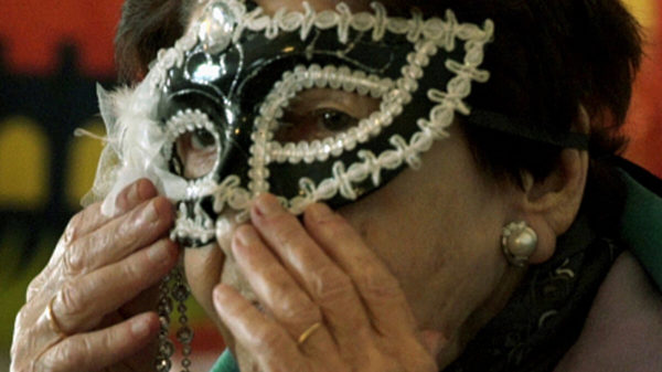 Eine ältere Frau setzt sich eine Faschings-Maske auf.