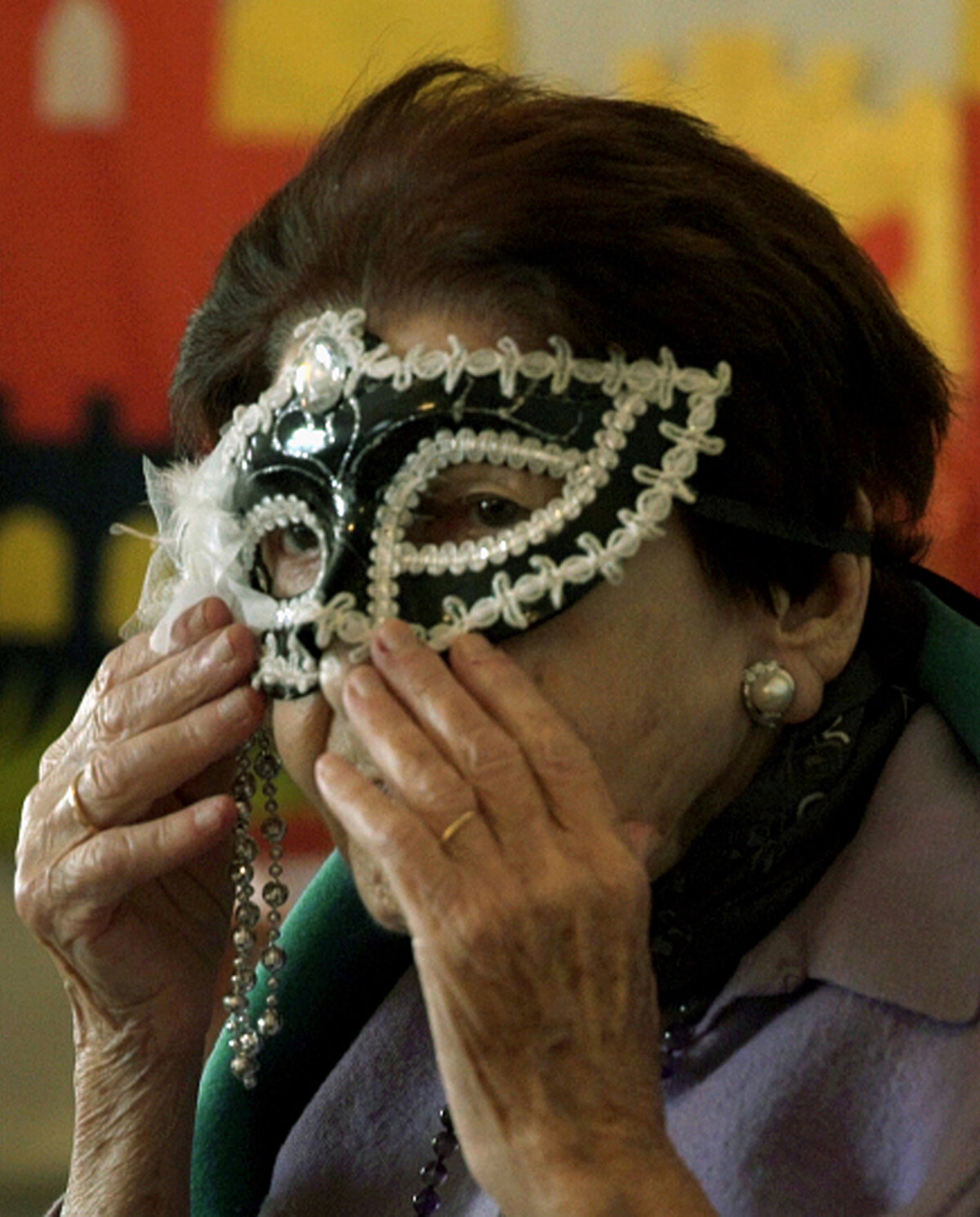 Eine ältere Frau setzt sich eine Faschings-Maske auf.