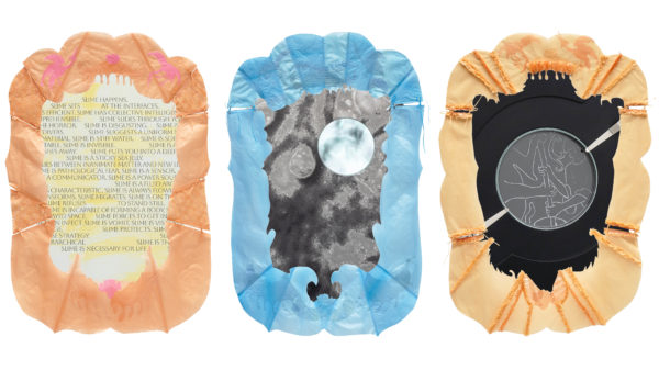 Drei nebeneinander angeordnete, organisch geformte Arbeiten mit textilen und plastischen Elementen: Links eine beige-rosafarbene Form mit eingespanntem Textfeld, in dem mehrfach das Wort „Slime“ erscheint. In der Mitte eine blau gerahmte Form mit einer grauen, fleckigen Oberfläche und einem runden, spiegelartigen Element. Rechts eine gelblich-beige Arbeit mit ausgefransten Rändern und einer zentralen runden Stickerei auf dunklem Grund, die eine figurative Szene zeigt.