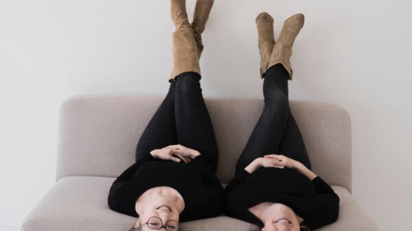 Deaf-Performerinnen Ilknur Warnecke und Susanne Kermer sitzen nebeneinander und kopfüber auf einem Sofa und lächeln.