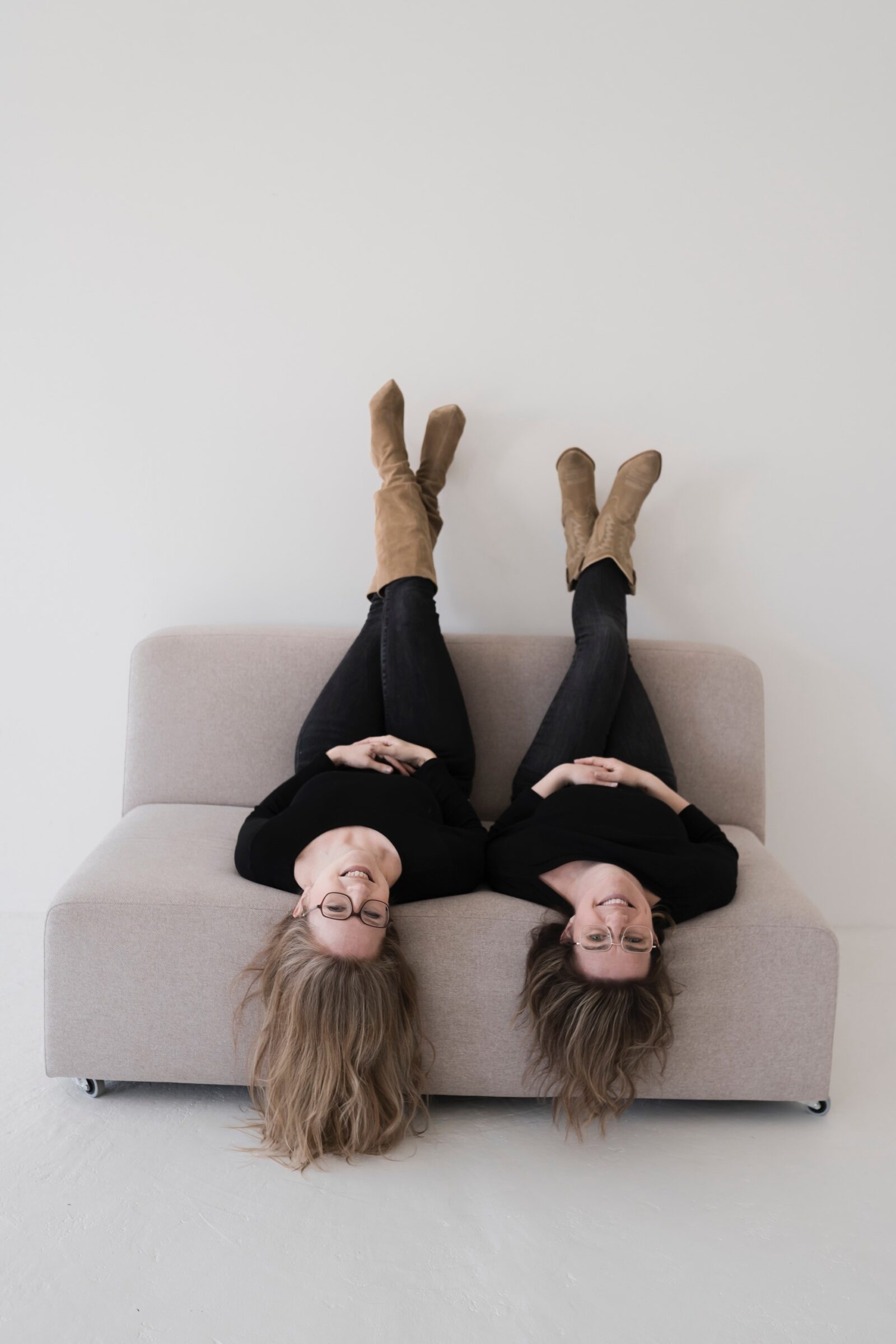 Deaf-Performerinnen Ilknur Warnecke und Susanne Kermer sitzen nebeneinander und kopfüber auf einem Sofa und lächeln.